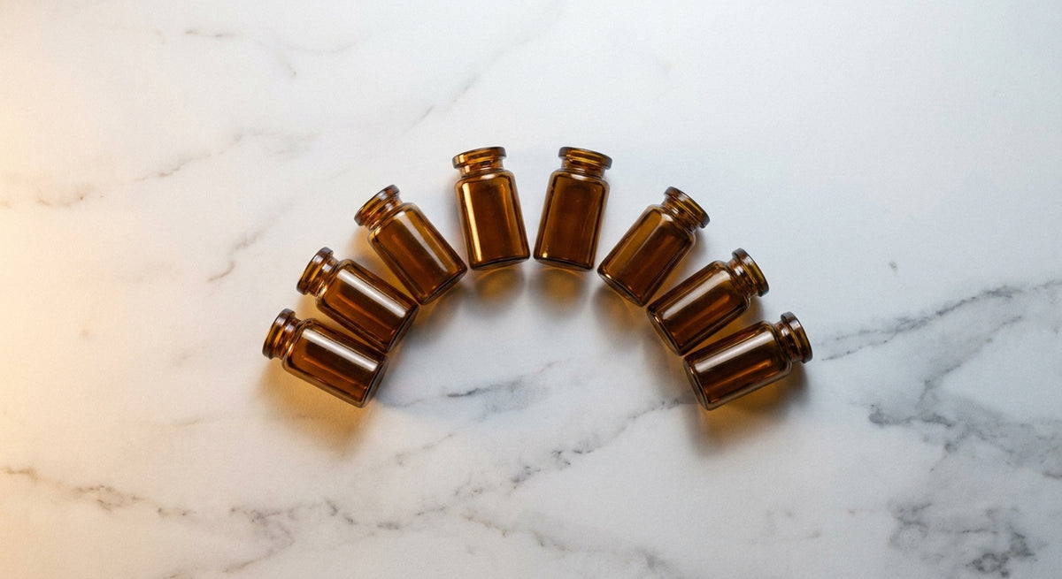 Six amber glass vials arranged in a clean arc on white marble under soft clinical lighting, evoking micronutrient diagnostics and precision health.